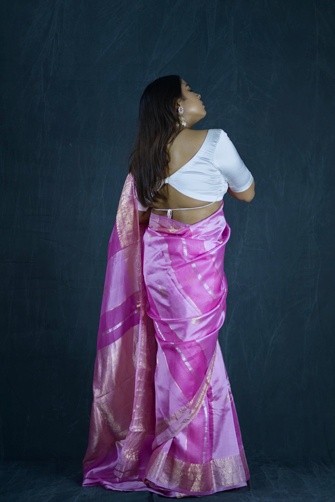 Woman wearing a white blouse and pink saree against a dark background