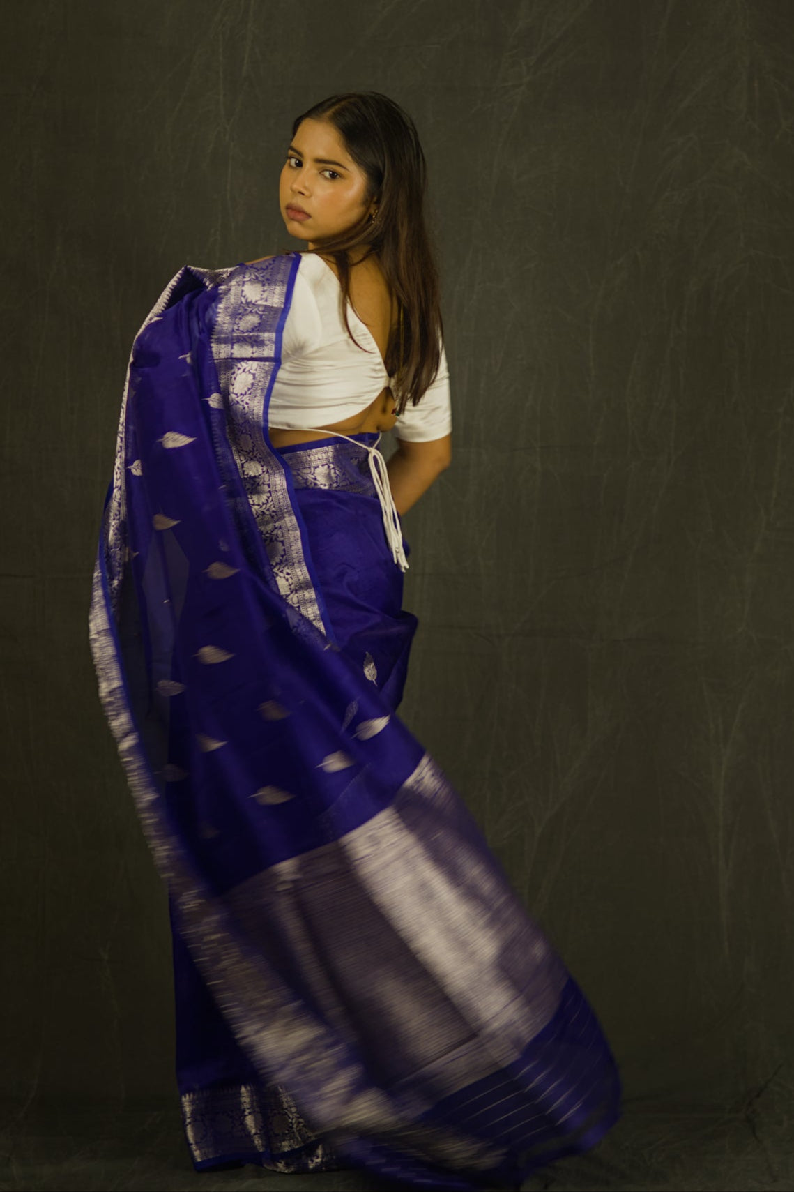 Woman wearing a blue and white saree against a dark background